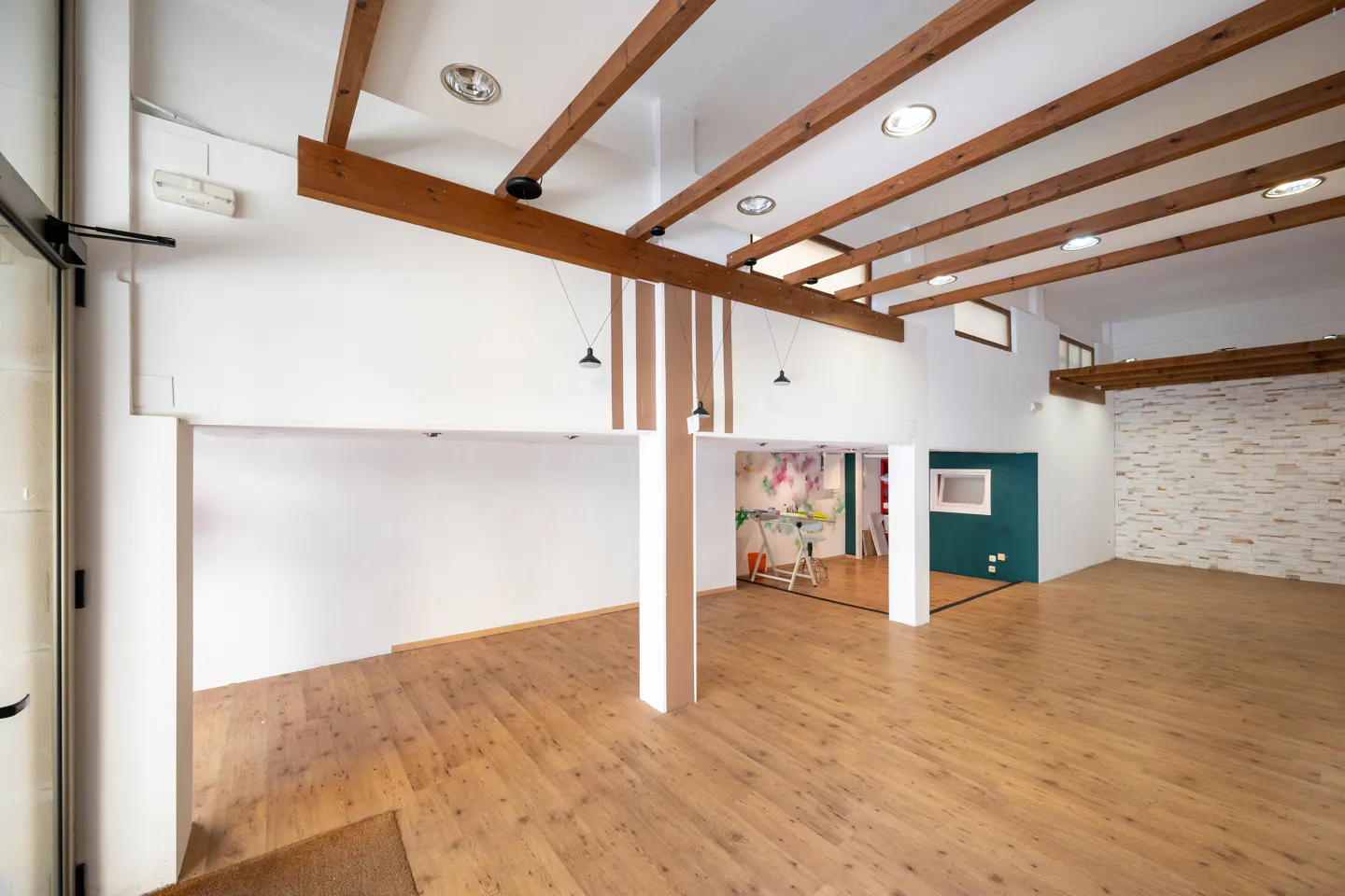 Bright, empty commercial space with wood floors, white walls, and exposed wood beams on the ceiling.