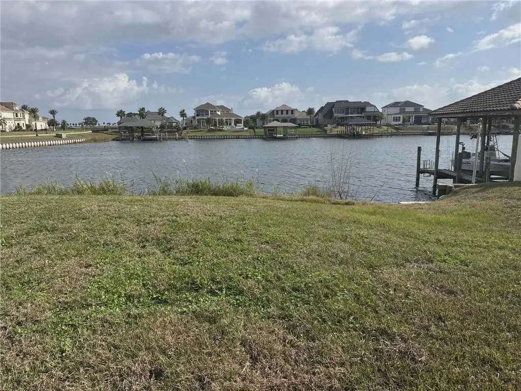 Waterfront property view with green lawn in foreground, canal, and luxury homes with boat docks in the background.