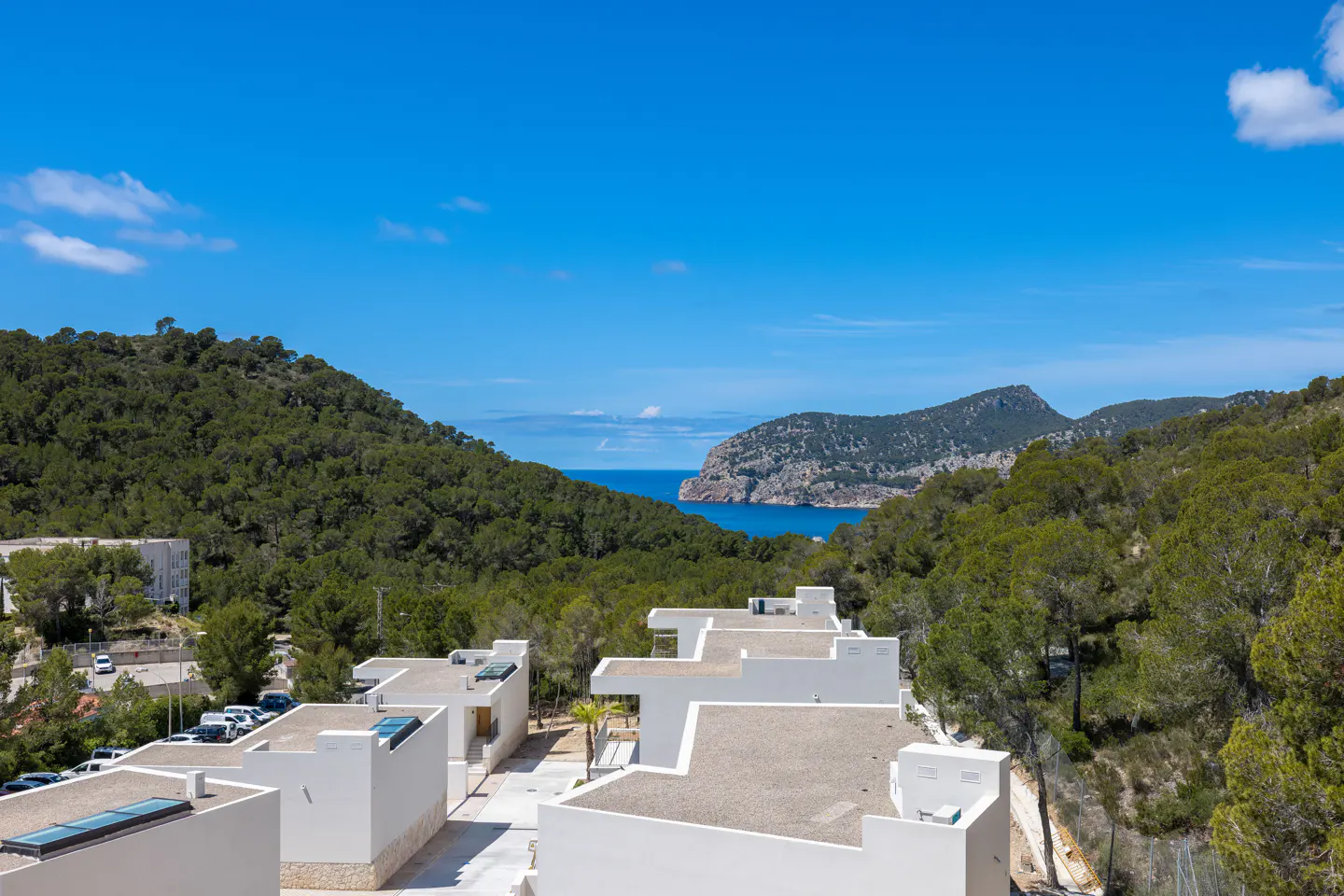 View of white modern villas nestled in green hills, overlooking the blue ocean and sky.