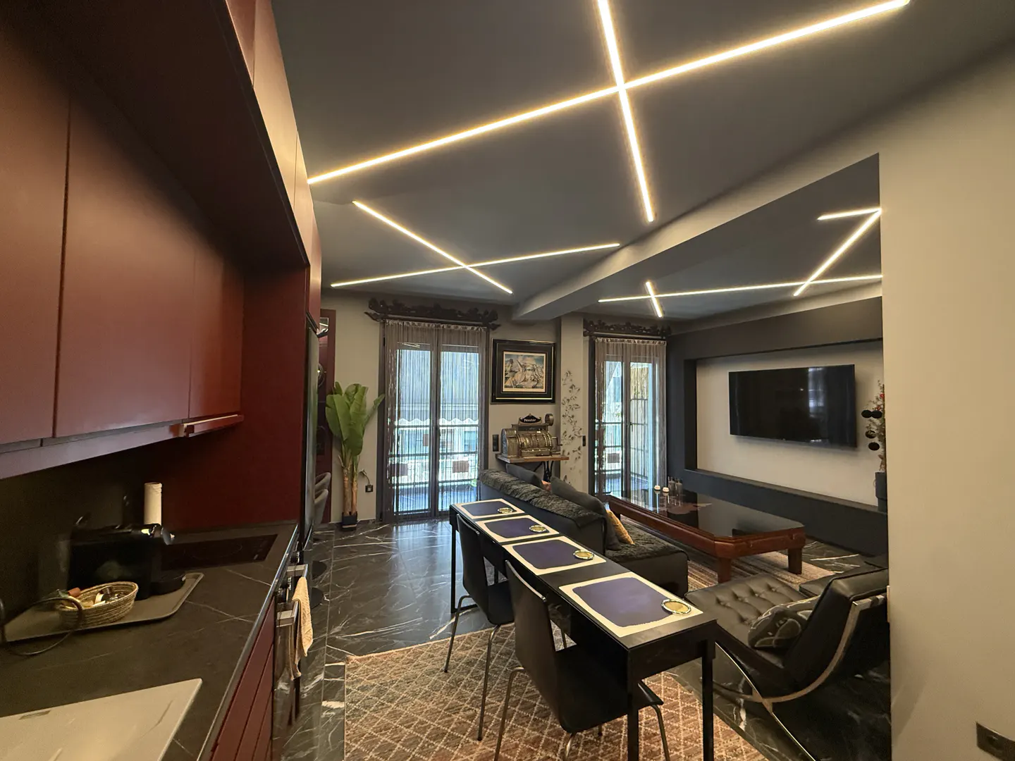 A modern living room with dark marble floors, a kitchen area, and unique ceiling lights.