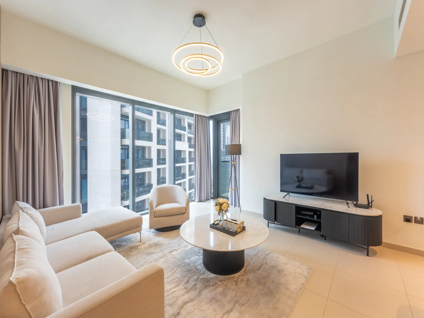 Bright living room with beige sofa, chair, and rug. A round marble table sits in the center, with a TV and console against the wall.
