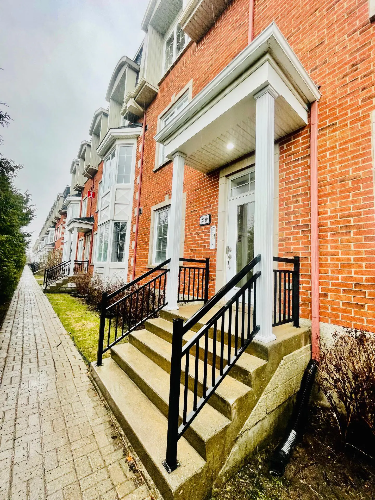 Row of red brick townhouses with white trim and black railings leading to front doors.