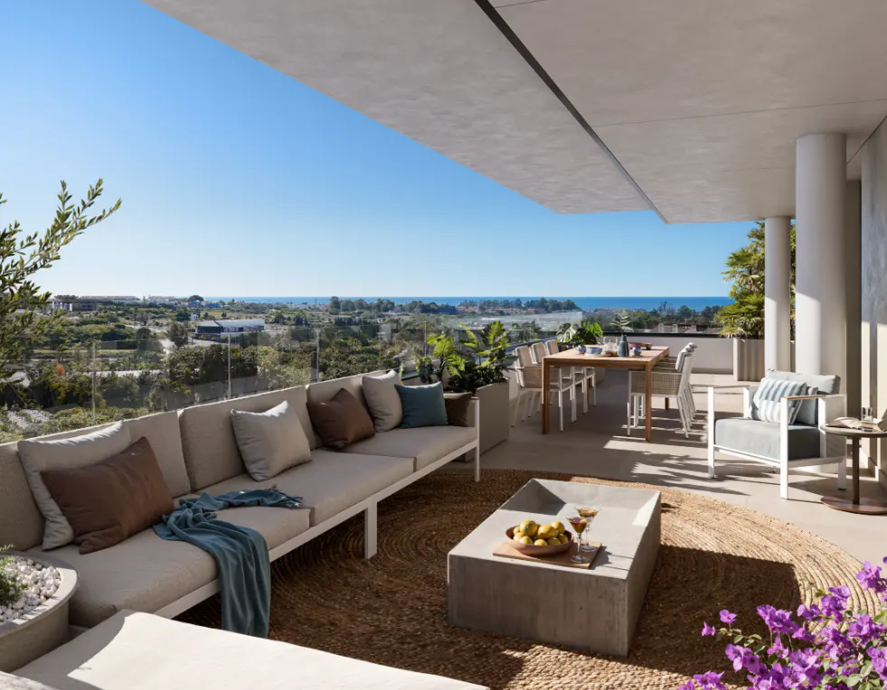 Luxury patio with beige sofa, concrete table, and dining set overlooking the ocean on a sunny day.