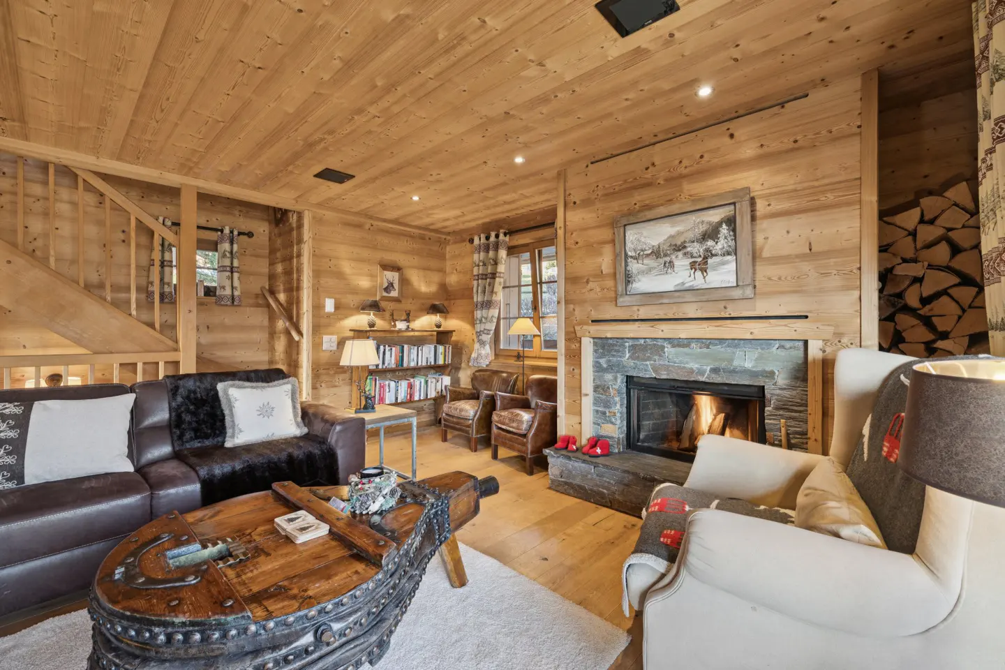 Cozy wood-paneled living room with leather sofas, stone fireplace with burning fire, and unique wooden coffee table.
