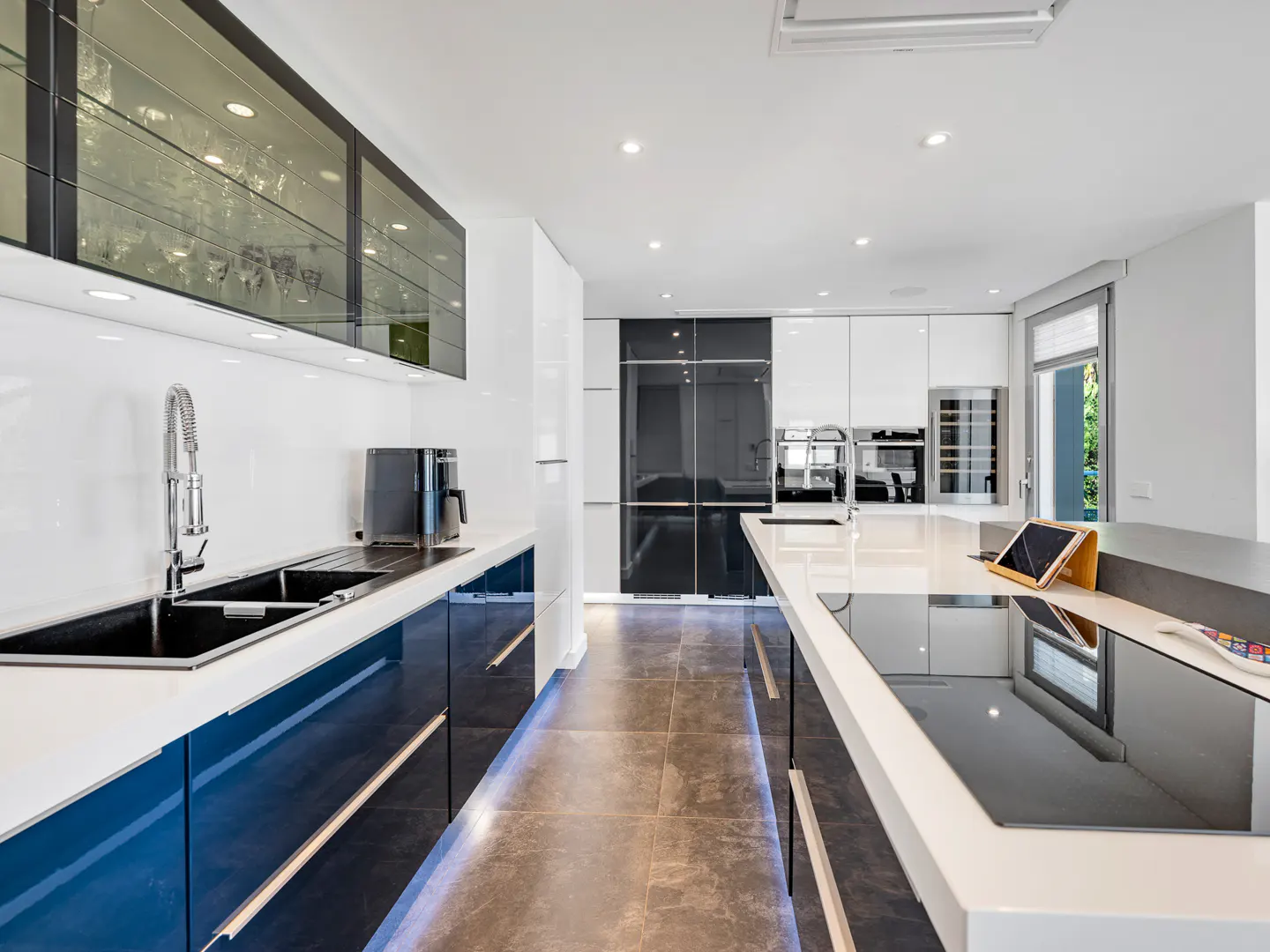 Modern kitchen with blue cabinets, white countertops, and stainless steel appliances. Island with cooktop and tablet.
