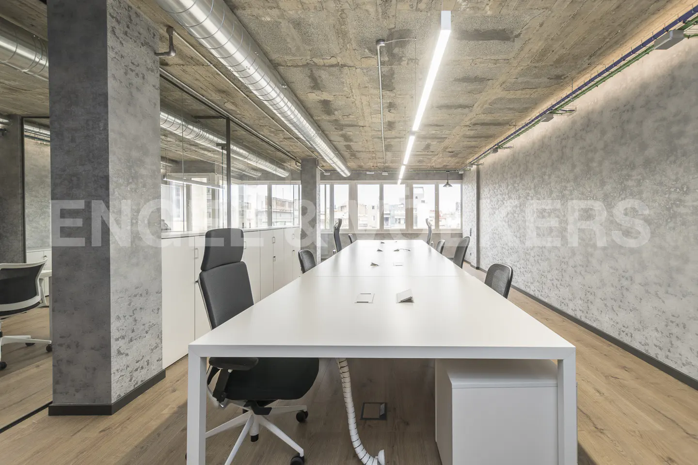Bright office space with a long white table, black chairs, concrete walls and ceiling, and wood floors.