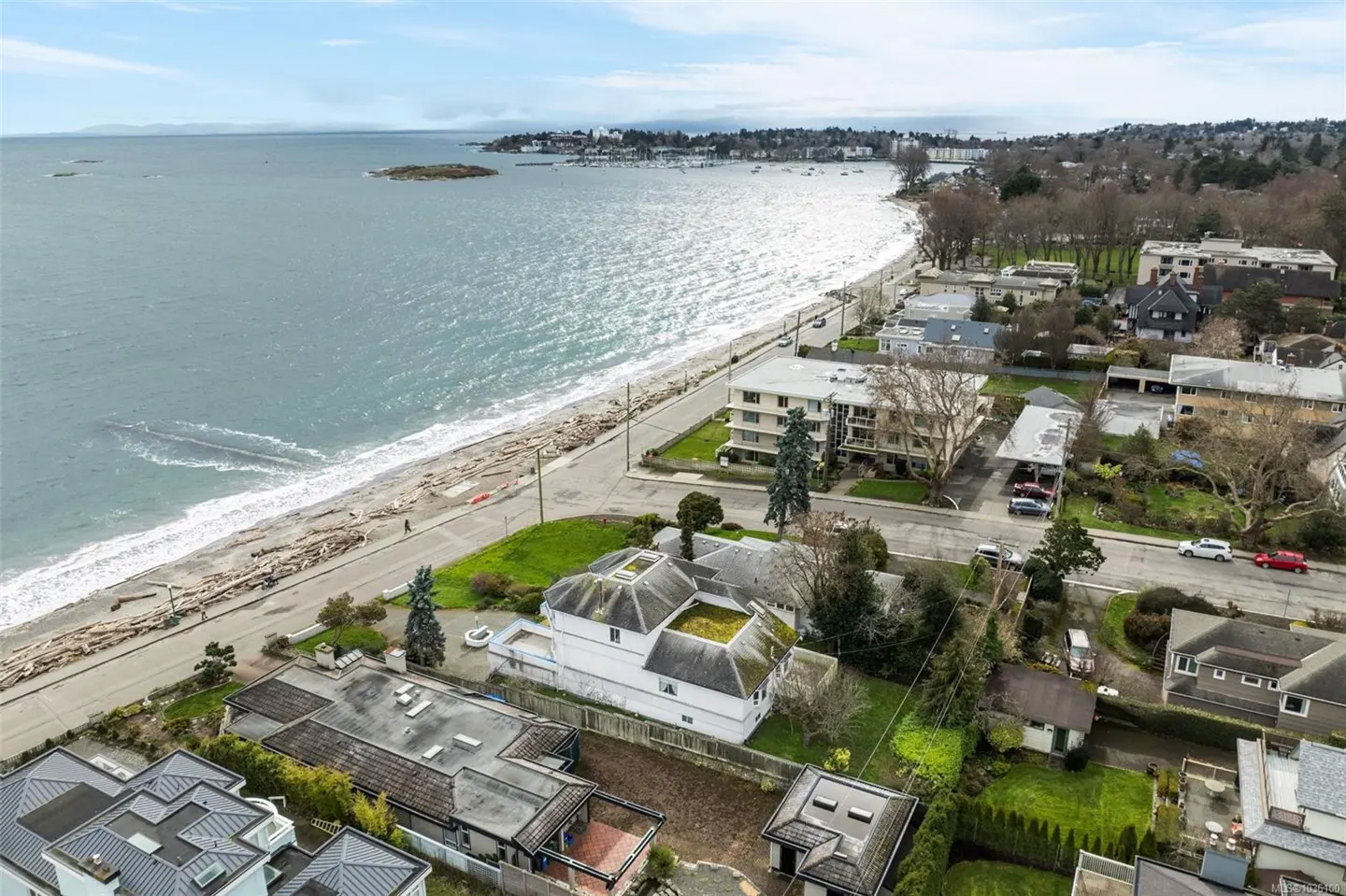 Aerial view of a white house with a green roof near a beach with driftwood and ocean.
