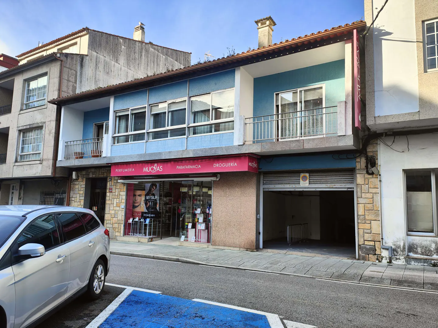 Street view of a two-story building with a blue facade above a storefront called "Muchas" with a garage door on the right.
