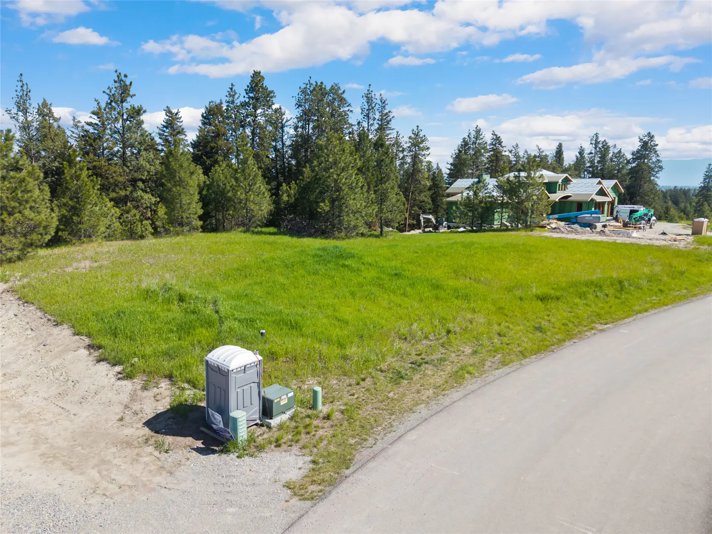 A grassy lot with a portable toilet and a house under construction in the background.