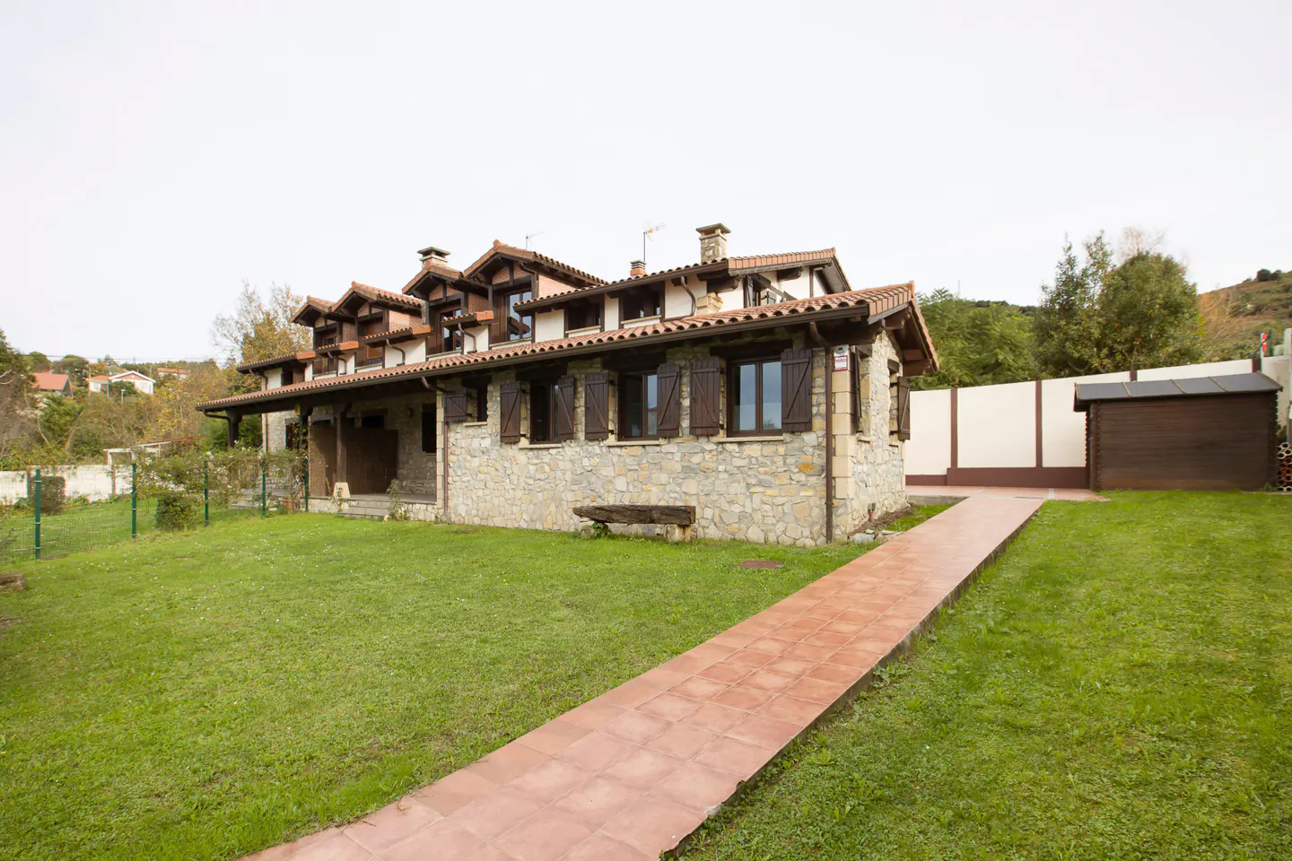 Stone house with brown shutters and a red tile roof. A red brick path leads to the house through a green lawn.