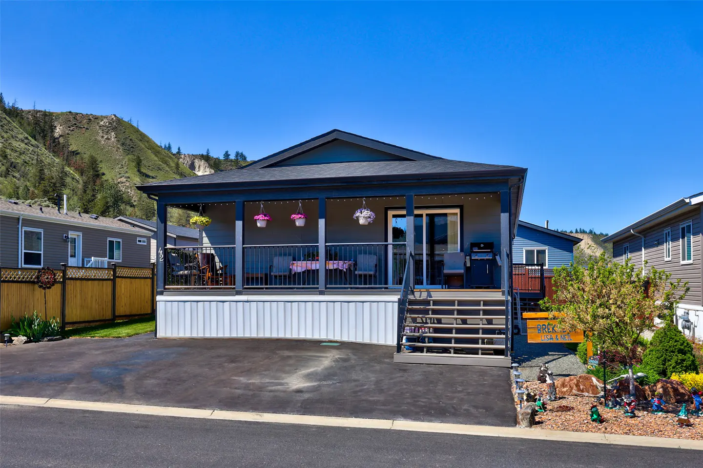 A single-story gray house with a covered porch, black trim, and a mountain backdrop on a sunny day.