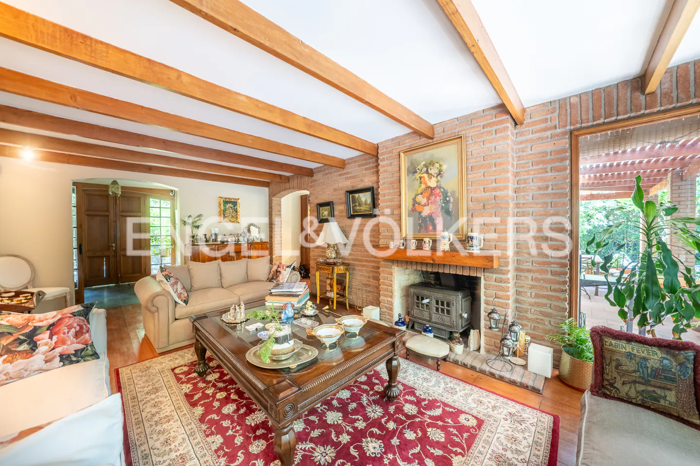 Living room with brick fireplace, wood beams, and a large rug. A sofa and coffee table are in the center of the room.