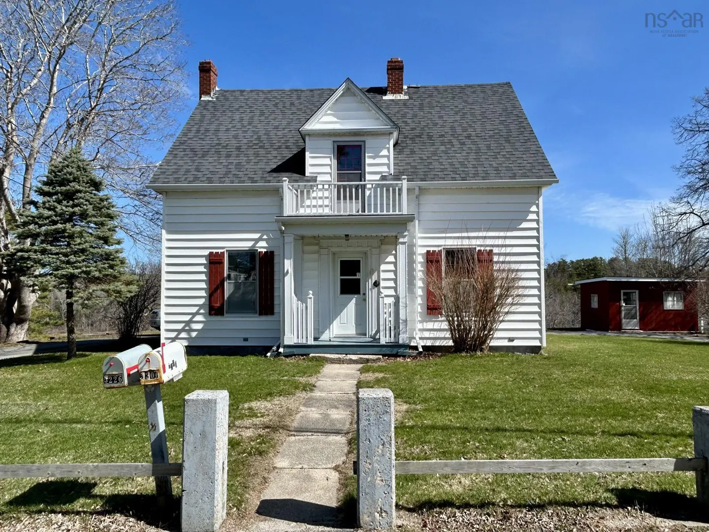 Two-story white house with red shutters and a gray roof on a sunny day. A stone path leads to the front door.