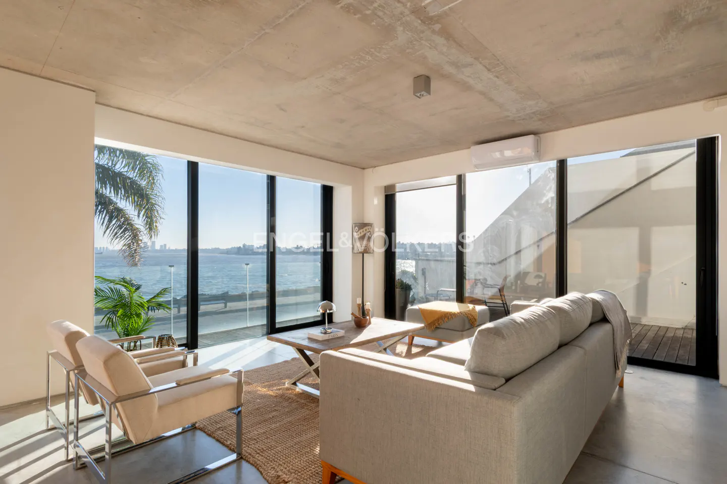 Living room with a gray sofa, two chairs, and a coffee table, with a view of the ocean through large windows.