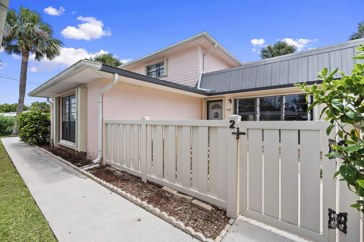Exterior view of a pink, two-story home with a white picket fence and a palm tree in the background.