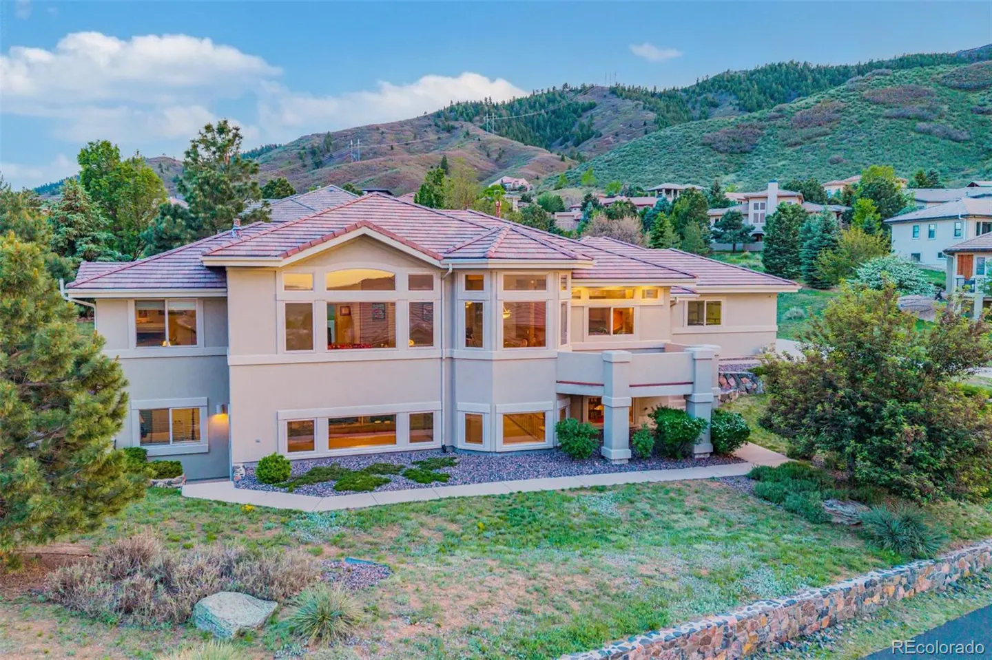 Beige two-story house with a red tile roof, many windows, and a mountain backdrop.