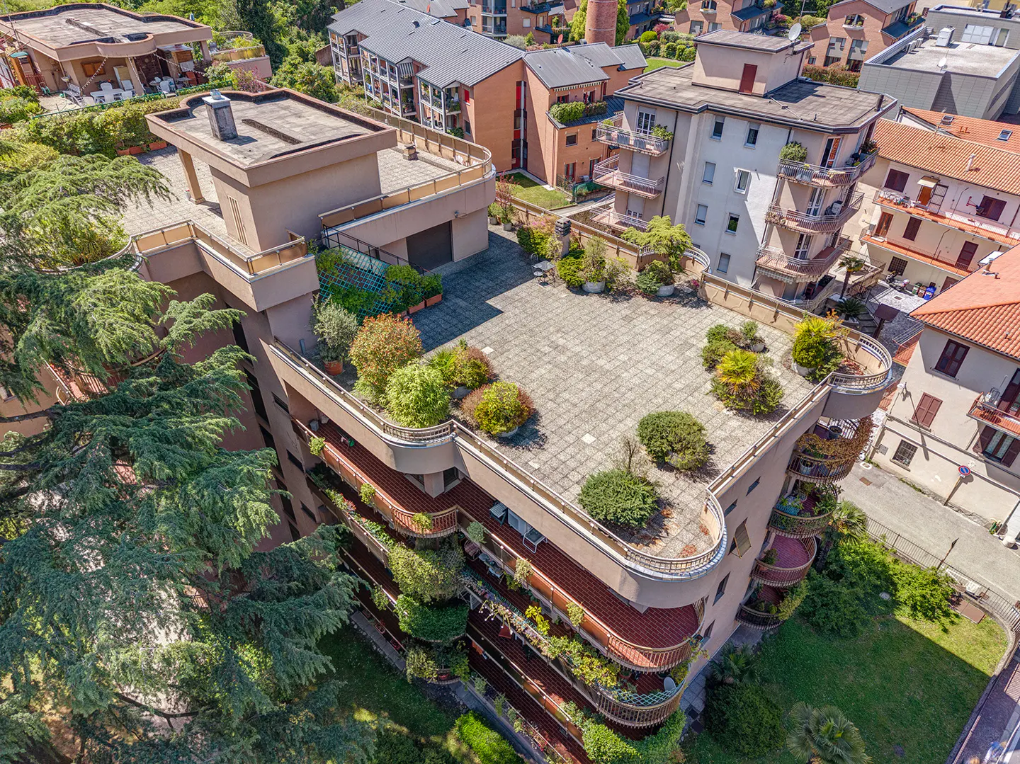 Aerial view of a multi-story apartment building with a rooftop terrace garden and curved balconies with plants.