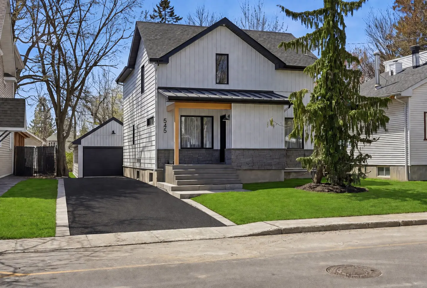 Exterior view of a two-story white house with a black roof, gray stone foundation, and a black asphalt driveway.