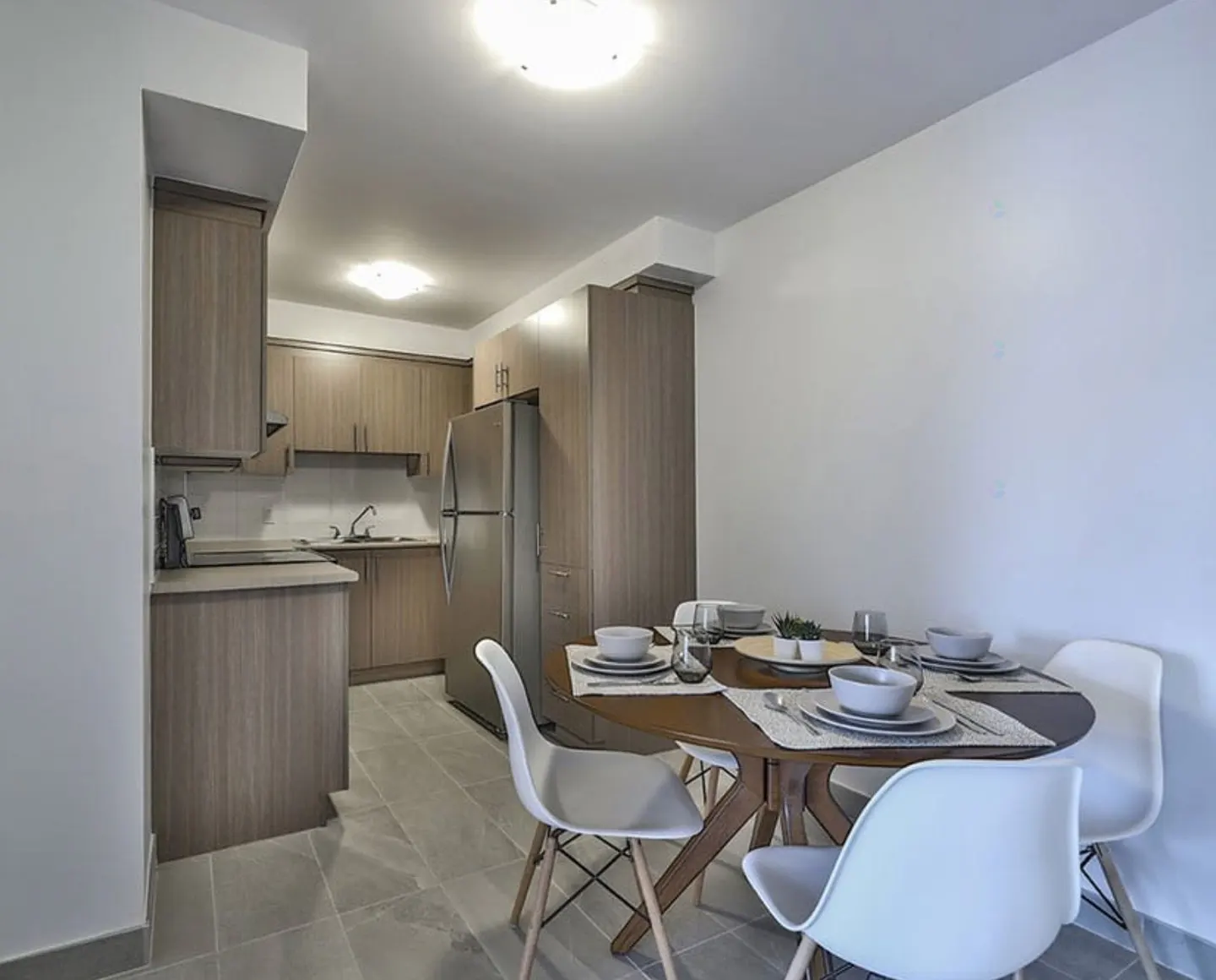 Modern kitchen with light wood cabinets, stainless steel fridge, and a round dining table with four white chairs.