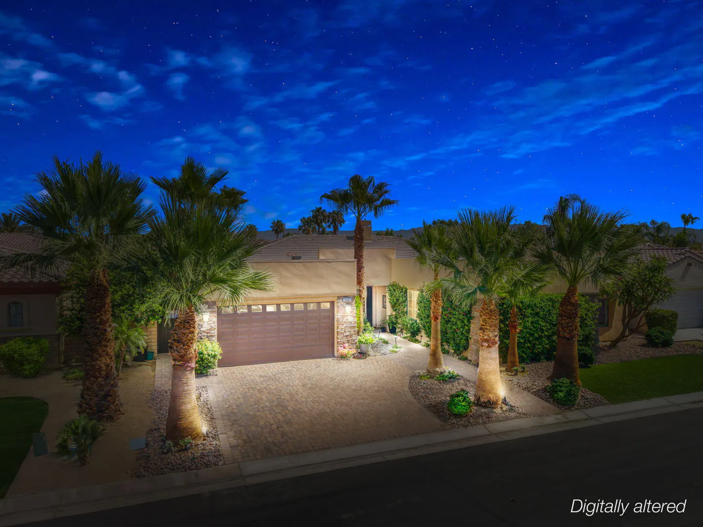 Single-story home with a paved driveway and palm trees at night under a starry blue sky.