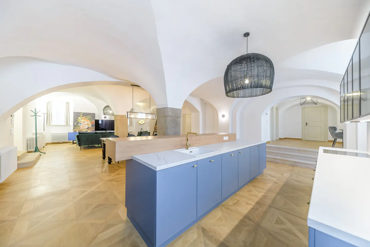 Open-concept kitchen and living room with arched ceilings, wood floors, and blue cabinets. A black wicker pendant light hangs above the island.