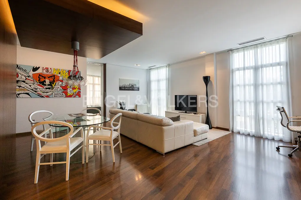 Open-concept living space with wood floors, a glass table, white sofa, and a pop art painting.