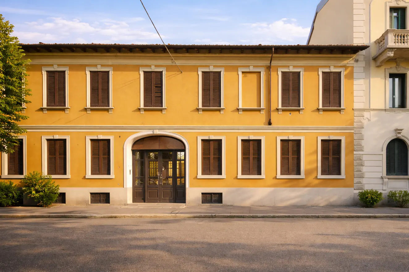 Two-story yellow building with brown shutters and a dark brown arched doorway, next to a white building.