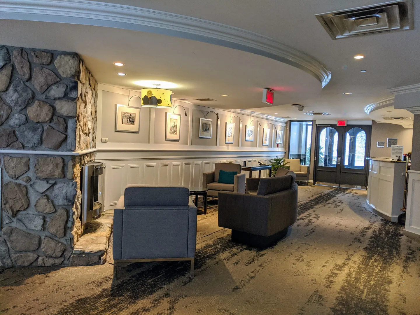 Hotel lobby with stone wall, gray sofas, and framed art. A reception desk and double doors are visible in the background.