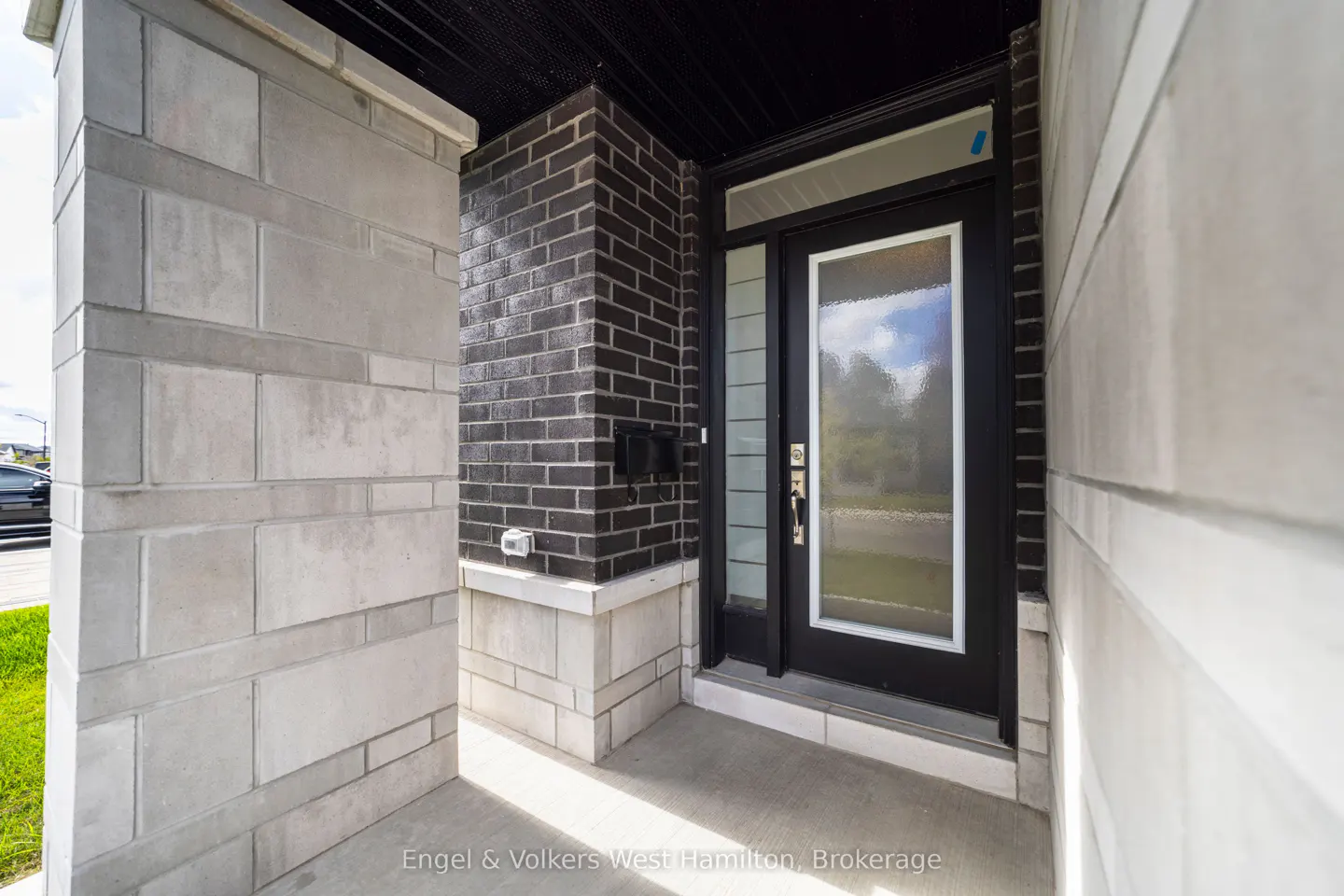 Front entrance of a home with a black door and white trim, brick and stone exterior, and concrete porch.