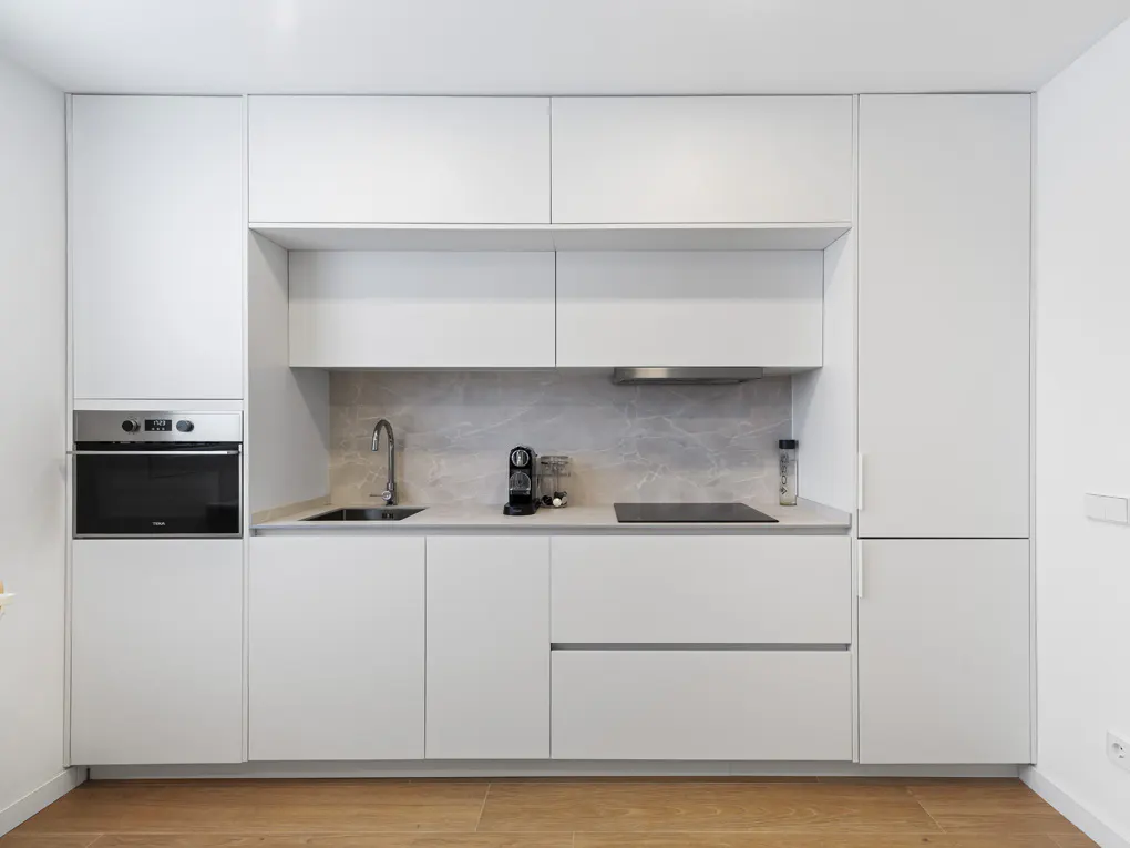 A modern kitchen with white cabinets, stainless steel appliances, and a light gray marble backsplash. A wood floor is visible.