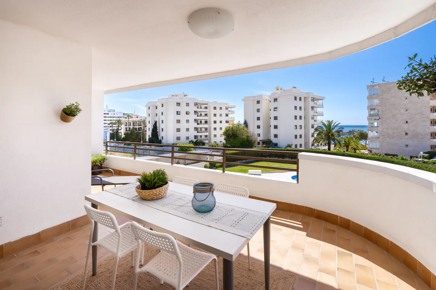 Balcony with white table, chairs, and decor overlooking buildings and blue sky.
