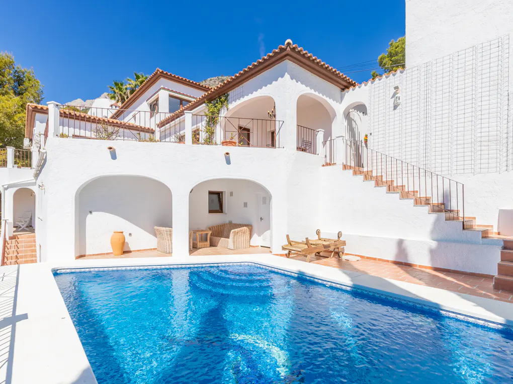 Exterior of a white villa with a blue swimming pool and terracotta roof tiles.