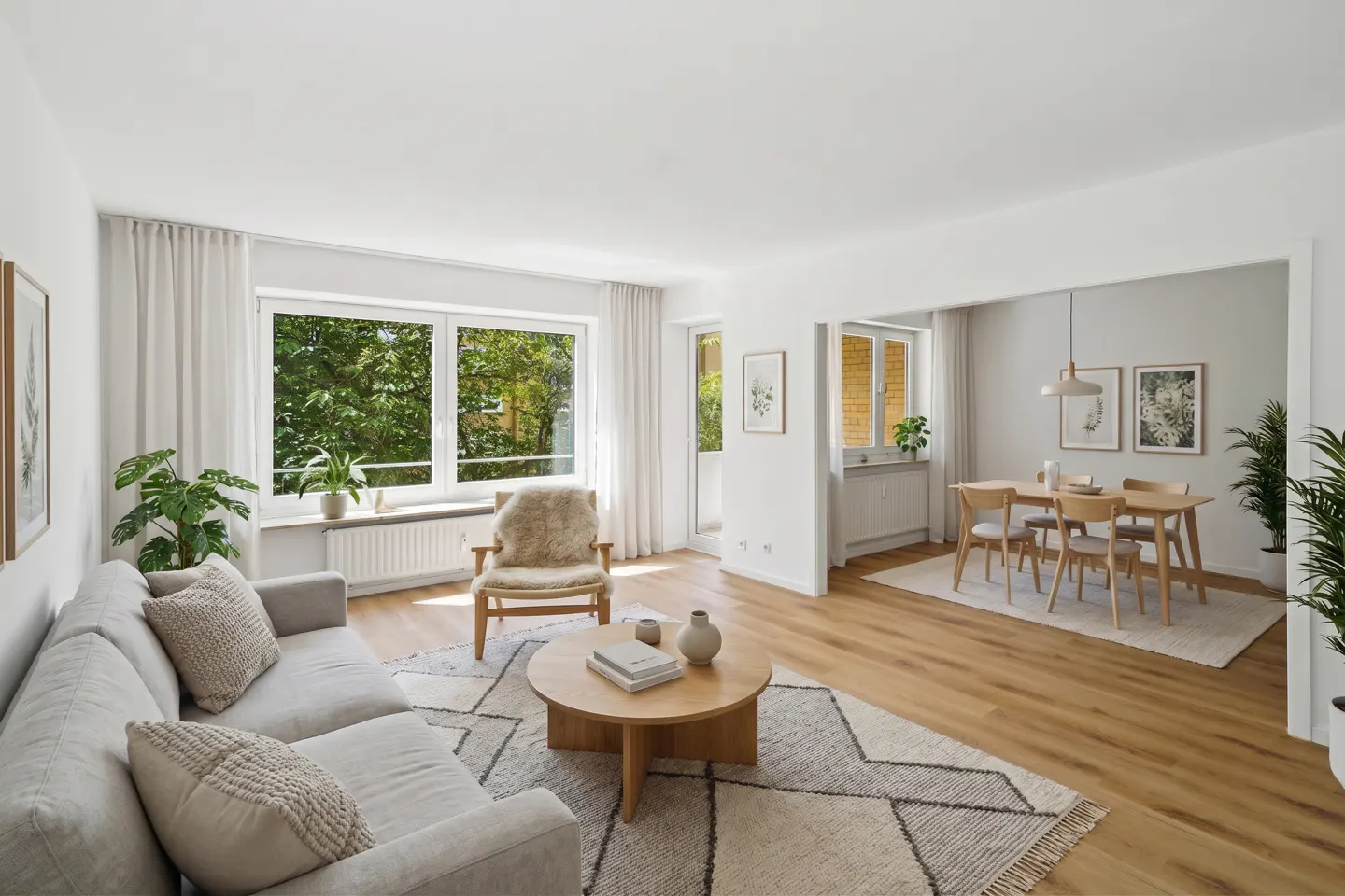 Bright, open-plan living and dining area with light wood floors, a grey sofa, round coffee table, and dining set.