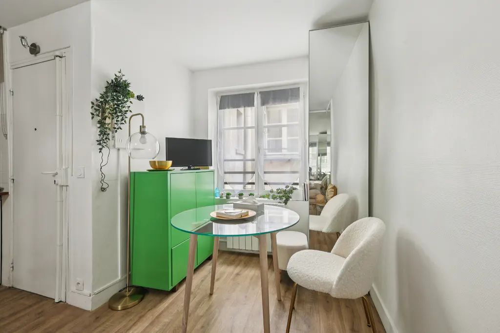 A small apartment interior with a glass table, two white chairs, and a green cabinet under a TV.