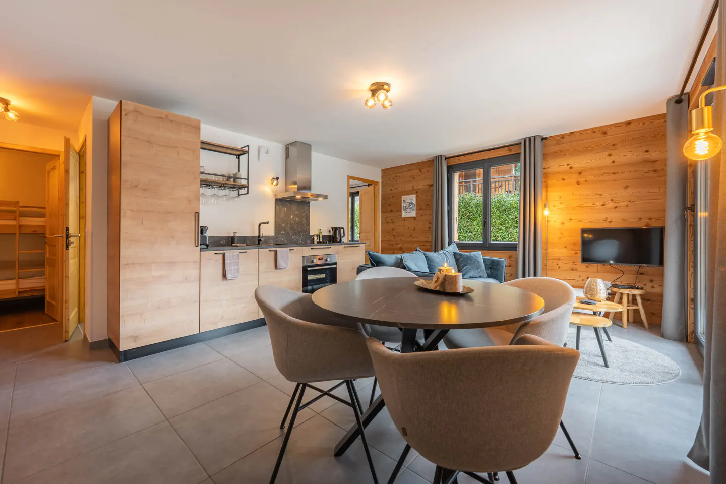 Open-concept living space with wood walls, a kitchen with light wood cabinets, and a round dining table with beige chairs.