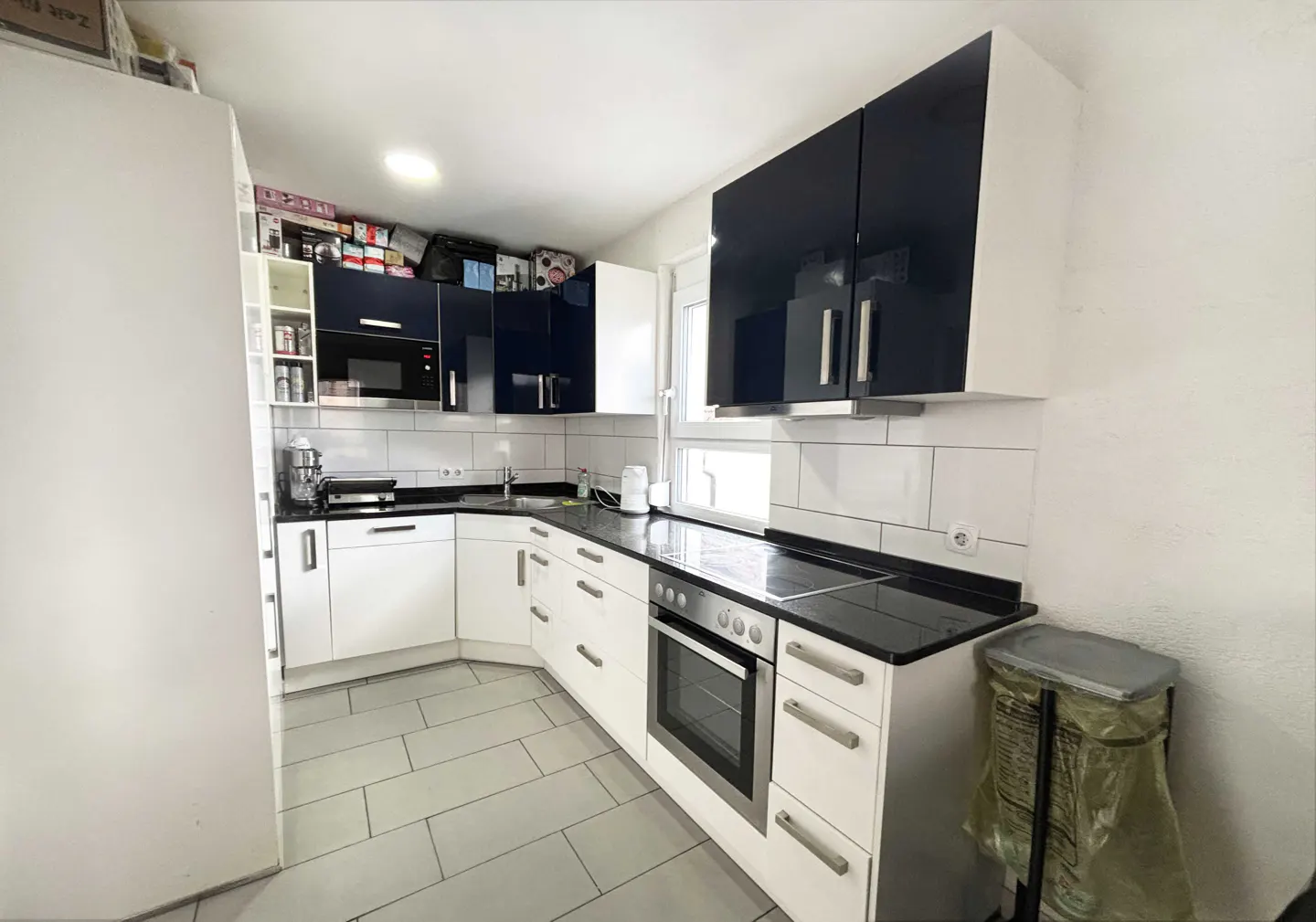 A modern kitchen with white cabinets, black countertops, and blue upper cabinets. A stainless steel oven is visible.