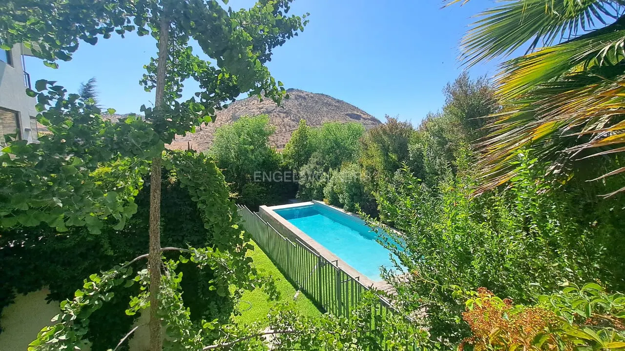 A rectangular pool with blue water is surrounded by green trees and a mountain under a blue sky.