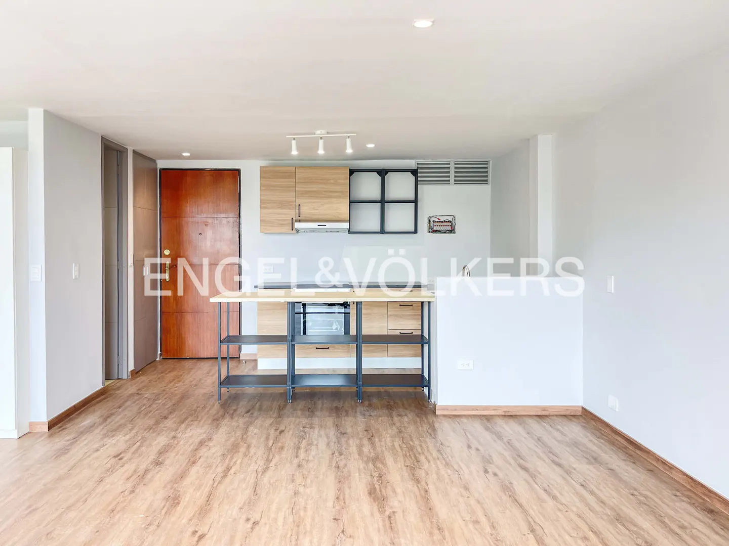 A bright, modern apartment interior with wood floors, a kitchen island, and light wood cabinets.