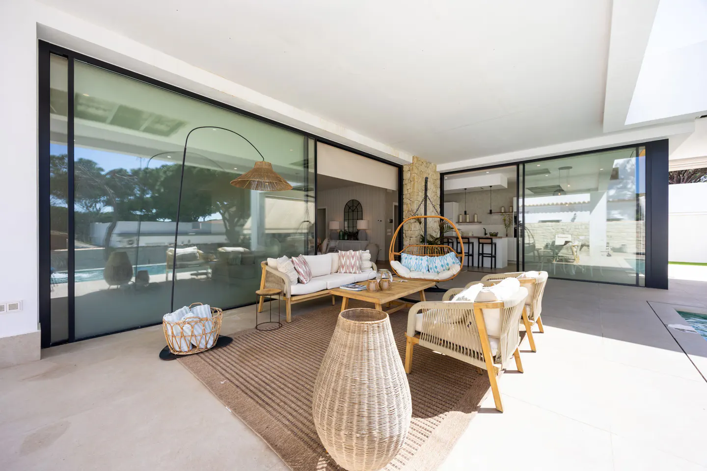 Outdoor patio with wicker furniture, including a sofa, chairs, and a hanging swing chair. Large sliding glass doors open to the interior.