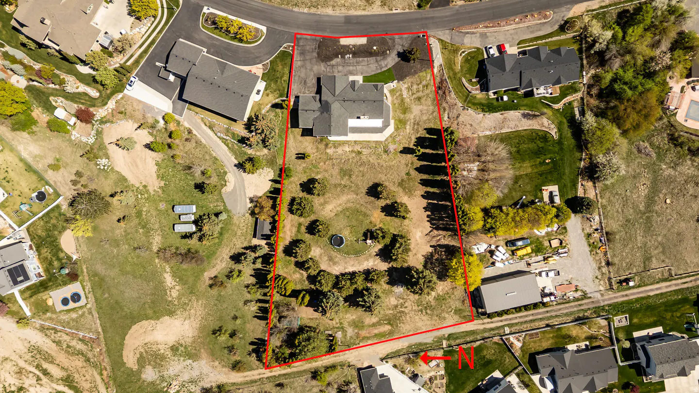 Aerial view of a property outlined in red, featuring a house, trees, and surrounding landscape.