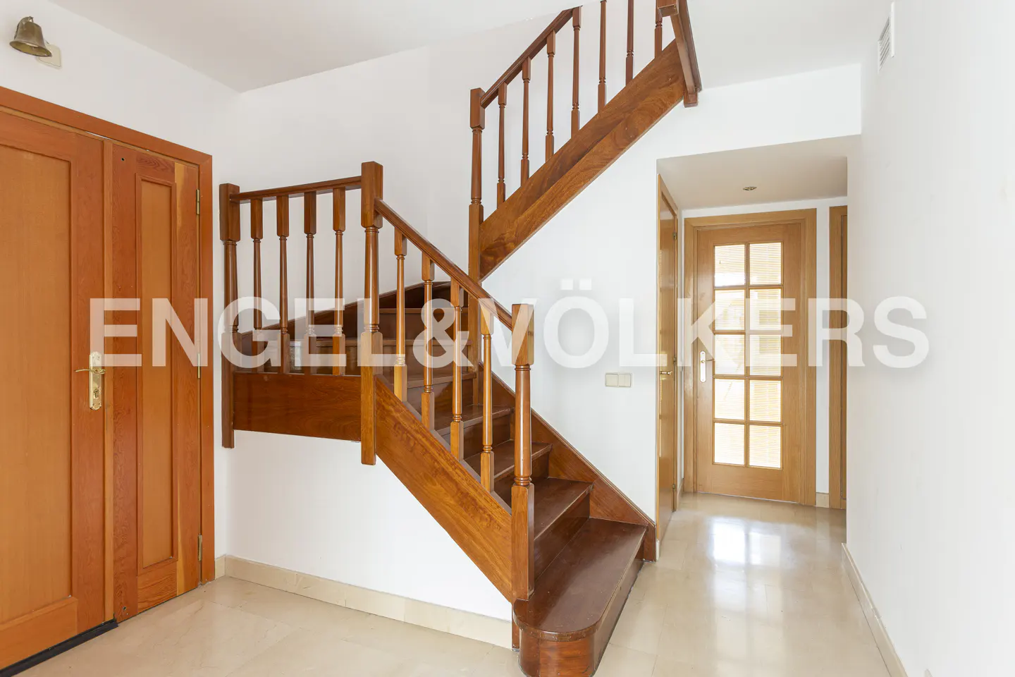 Interior view of a home featuring a wooden staircase, a closed wooden door, and a hallway with a glass-paneled door.