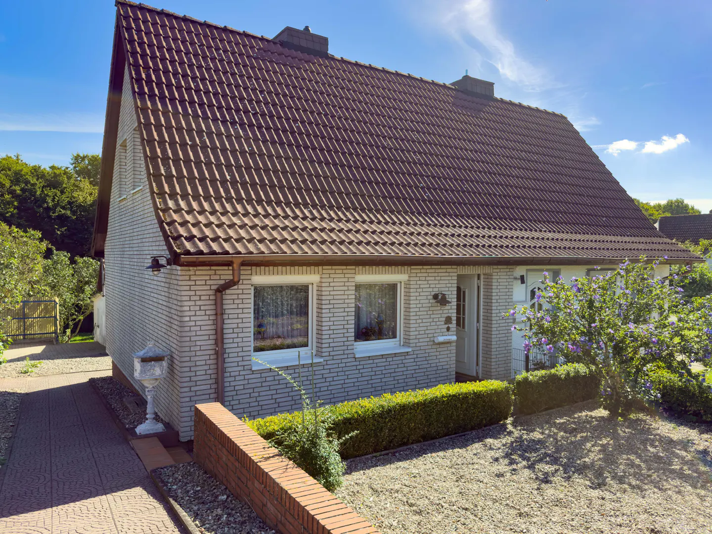 Exterior of a one-story white brick house with a brown tile roof and green landscaping.