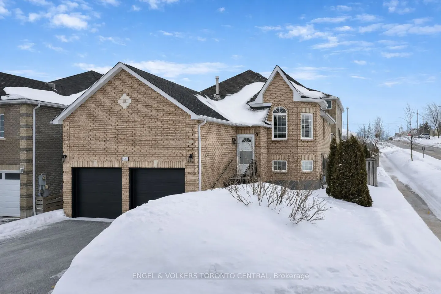 Two-story brick house with black garage doors and snow-covered lawn on a sunny winter day.