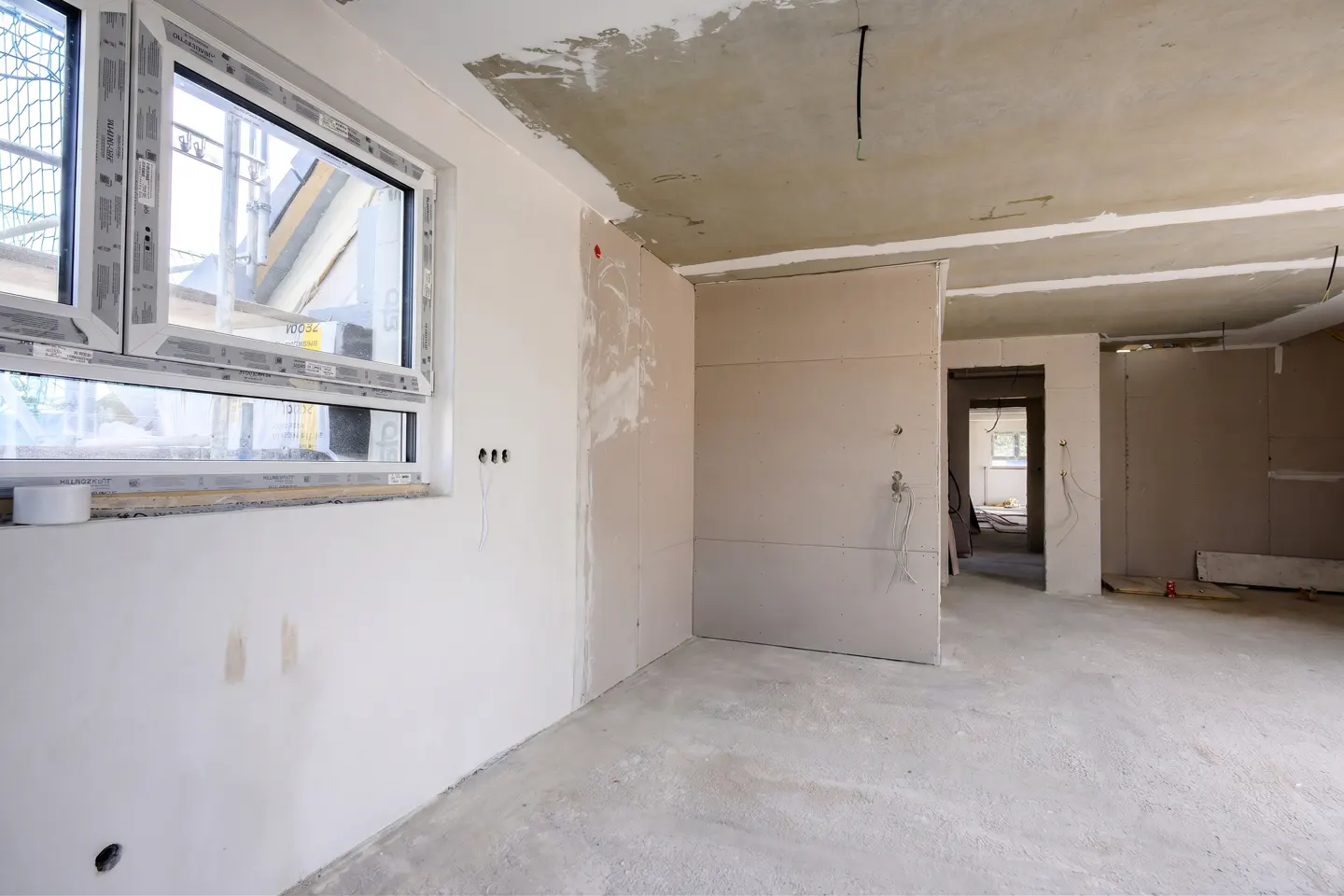 Unfinished room with white walls, a concrete floor, and a white window. Electrical wiring is visible. The room is under construction.