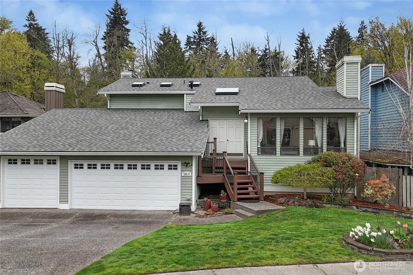 Exterior of a two-story, light green house with a gray roof, white garage doors, and a small front yard.