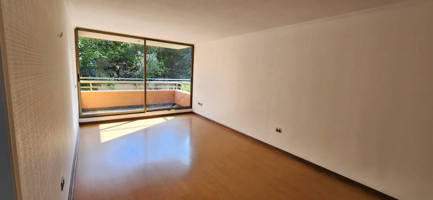 Empty room with light wood floors, white walls, and a sliding glass door to a balcony with green trees in the background.