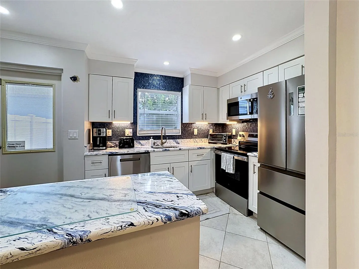 Modern kitchen with white cabinets, blue mosaic backsplash, stainless steel appliances, and blue-veined marble countertops.