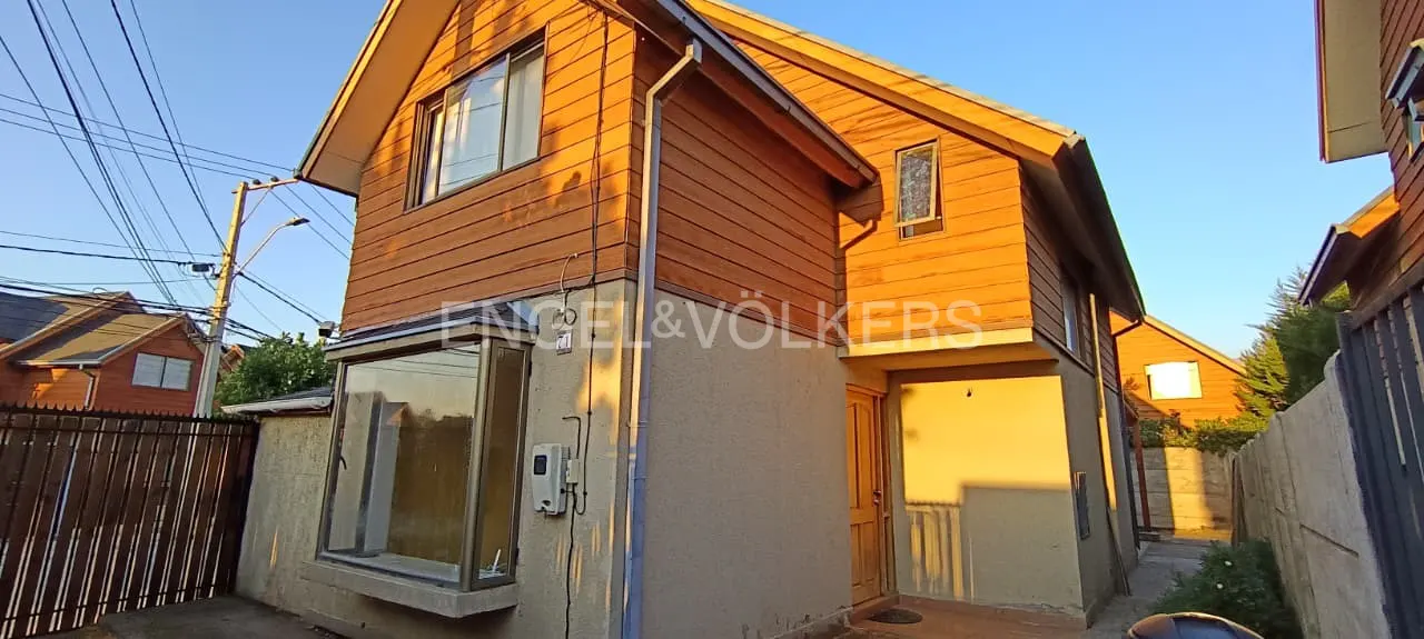 Two-story house with wood siding and a beige stucco base, under a blue sky. The Engel & Völkers logo is visible.