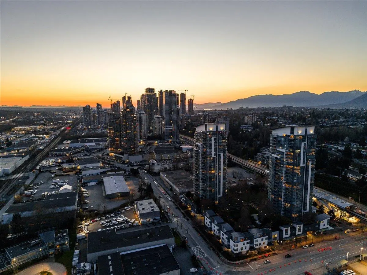Aerial view of a city skyline at sunset, featuring tall buildings, mountains, and a colorful sky.