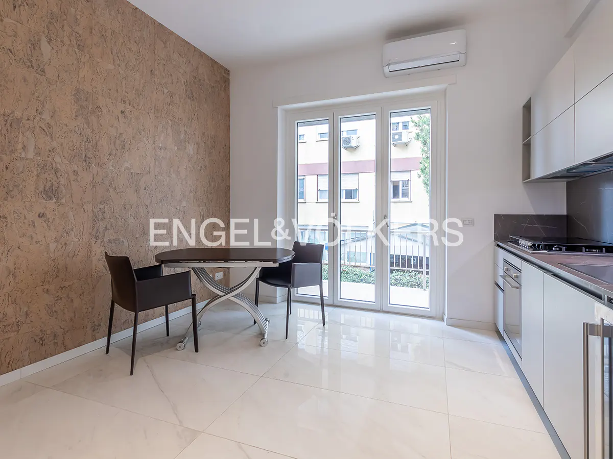 Modern kitchen with white cabinets, marble floors, a dining table with two chairs, and a textured brown accent wall.